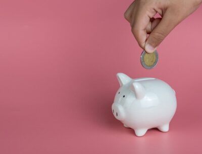 A hand placing a coin into a white piggy bank, symbolizing cost savings and affordable medical travel options with ROYAL MEDICAL.