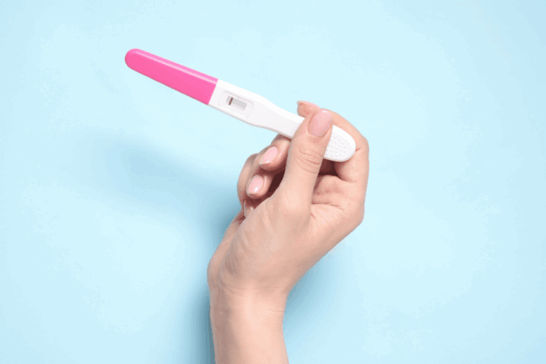 Hand holding a pregnancy test with a negative result on a light blue background.