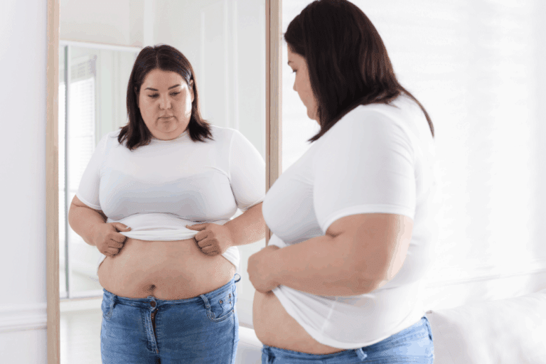 Woman looking at her abdomen in the mirror before abdominoplasty surgery, considering tummy tuck options for BMI 30+